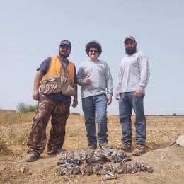 Three men standing next to a pile of dead birds at home.